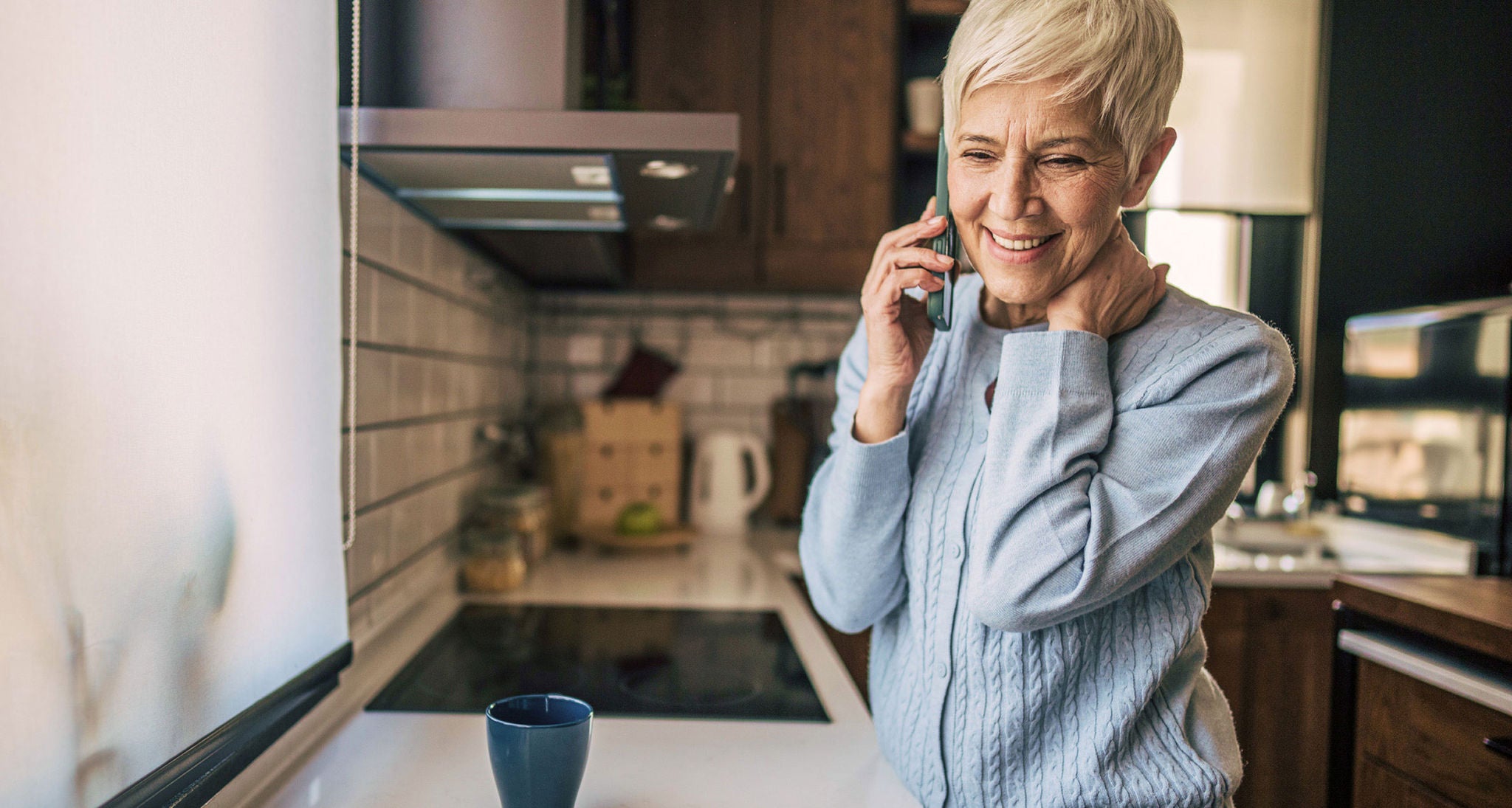 A smiling person talks on the phone in a kitchen.