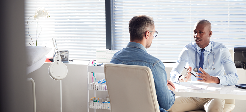 Physician speaks with patient at a desk in an office.