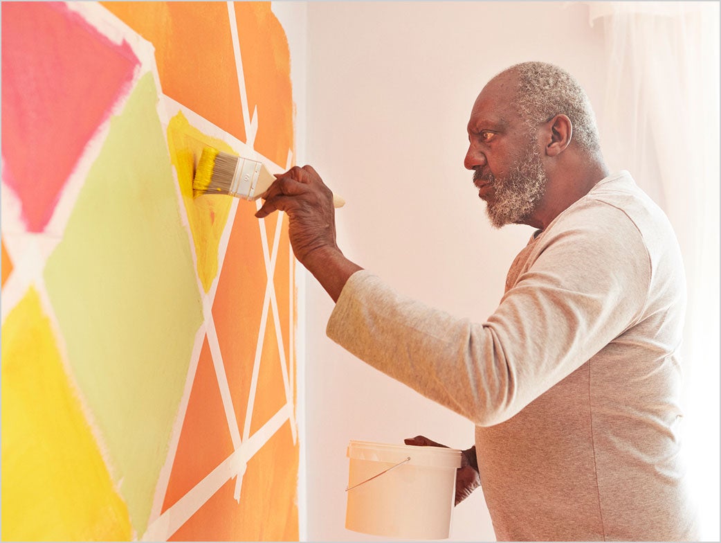 A person paints a colorful geometric design on a wall with a paintbrush.
