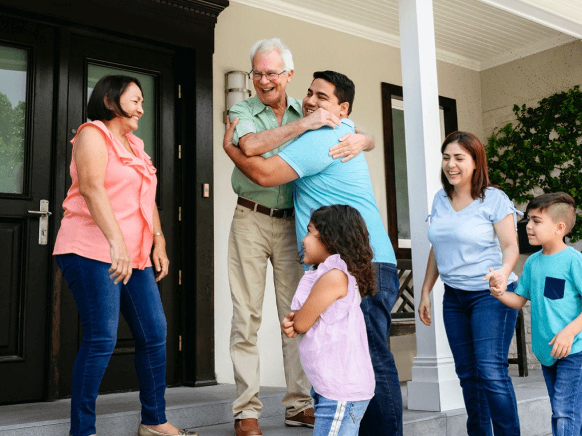 Family members laugh and hug as they greet each other on a front porch.