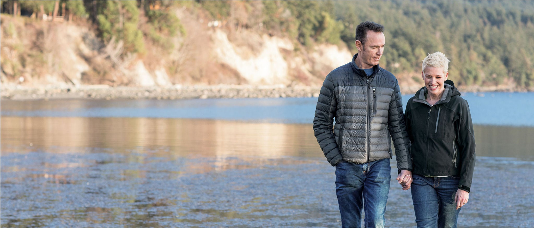 A woman in a black jacket smiles while pushing a wheelbarrow in a garden. 