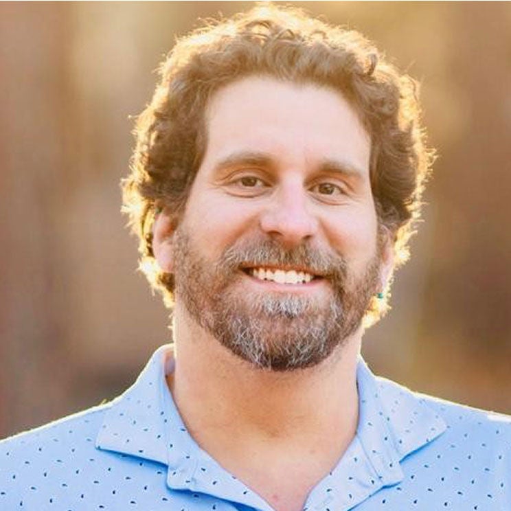 Dave N. smiles. With curly hair and a light blue shirt with small dots