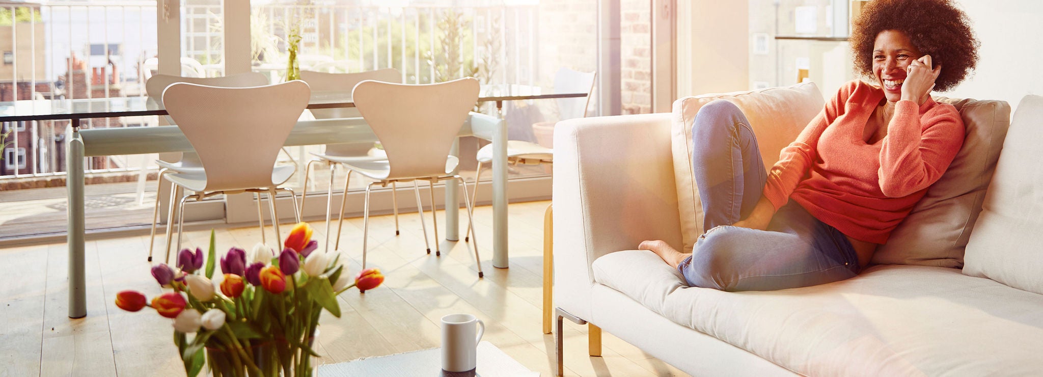 A person sits on a couch, smiling and talking on the phone.