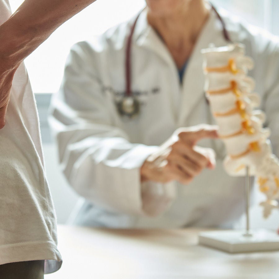 A doctor points to a spine model while a patient stands nearby.