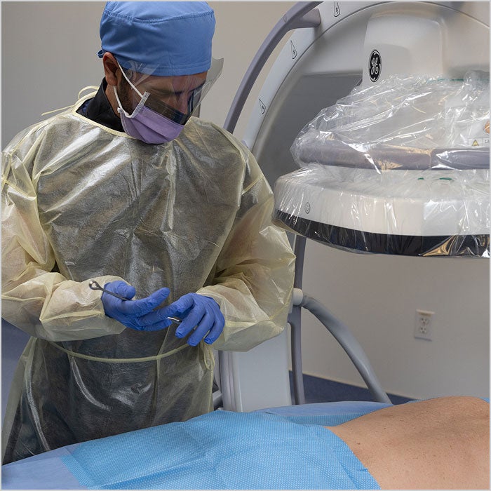 A healthcare worker in protective gear stands by a patient lying on a medical table. 
