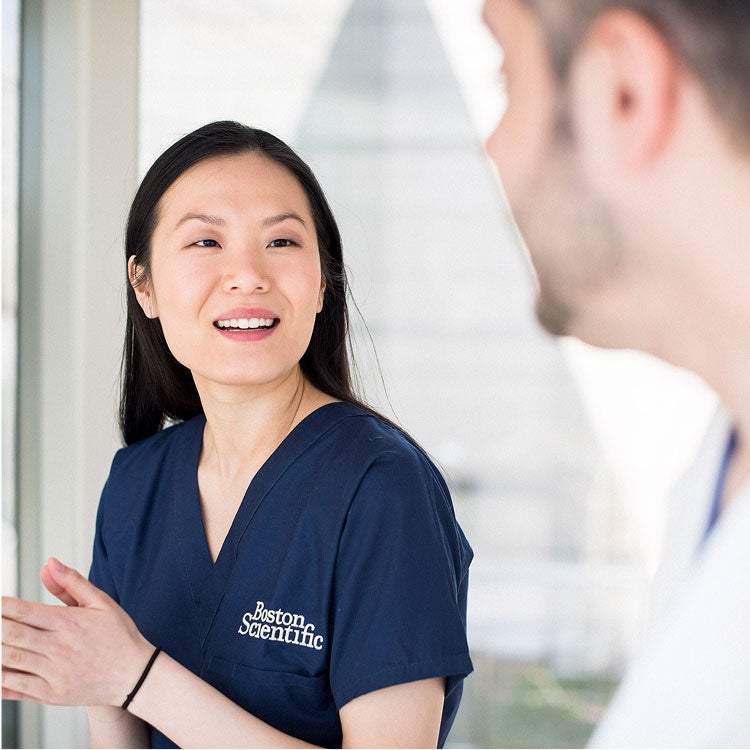 A person in Boston Scientific scrubs smiles while talking to another person.