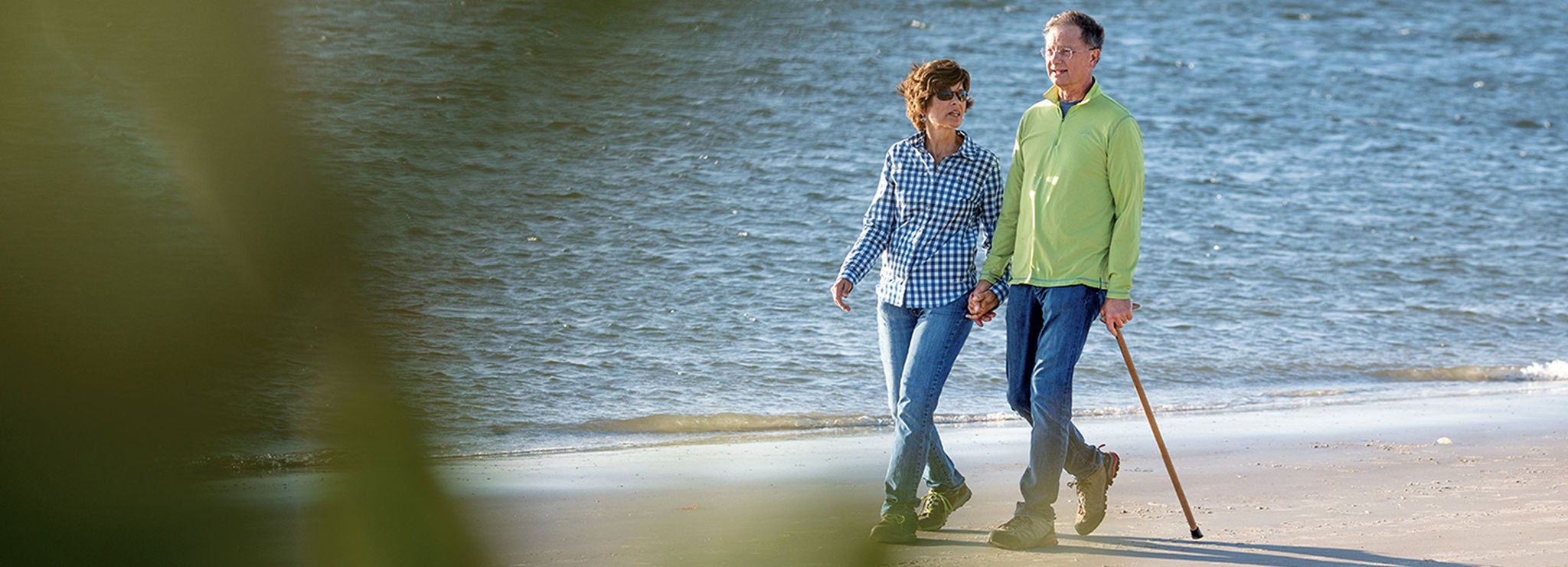 A couple walking hand in hand on the beach with gentle waves behind them.