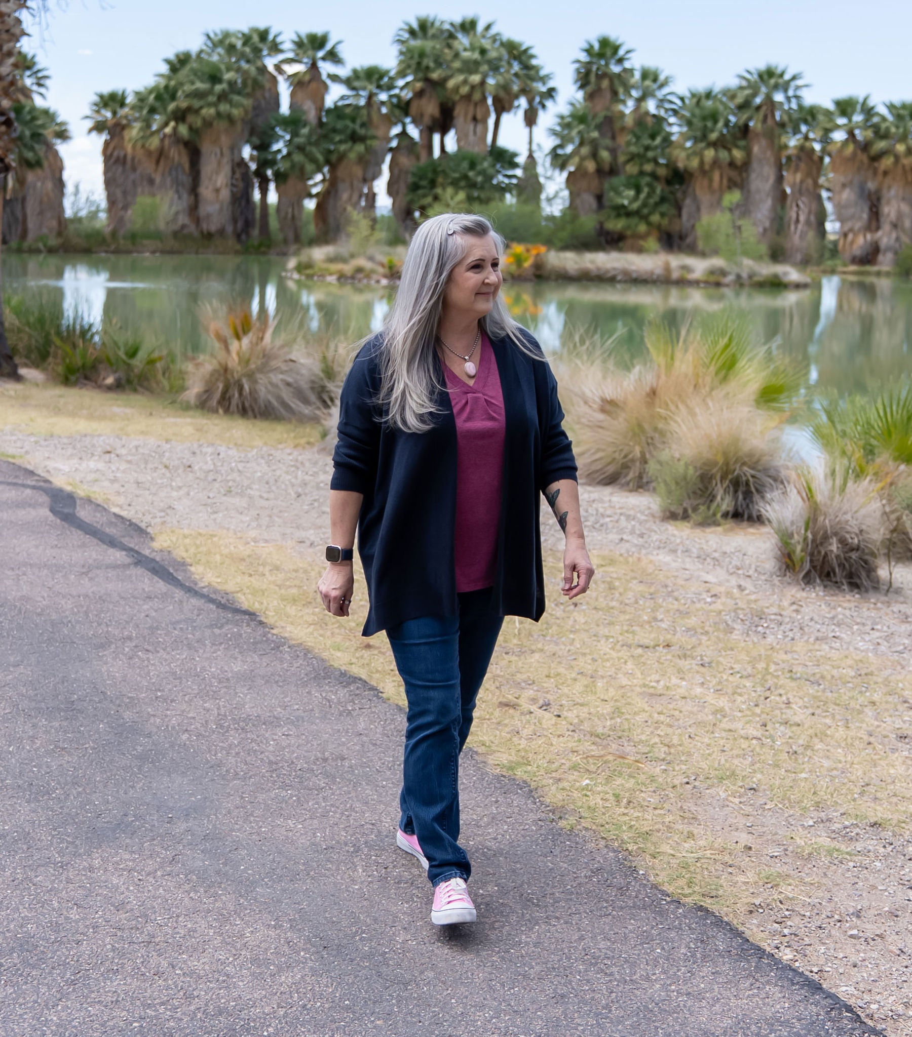 Woman walking beside a pond surrounded by palm trees.