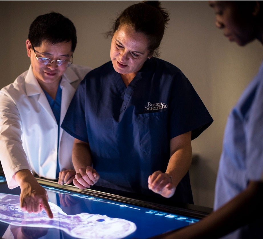 Three medical professionals analyze a digital display of a patient's spine.