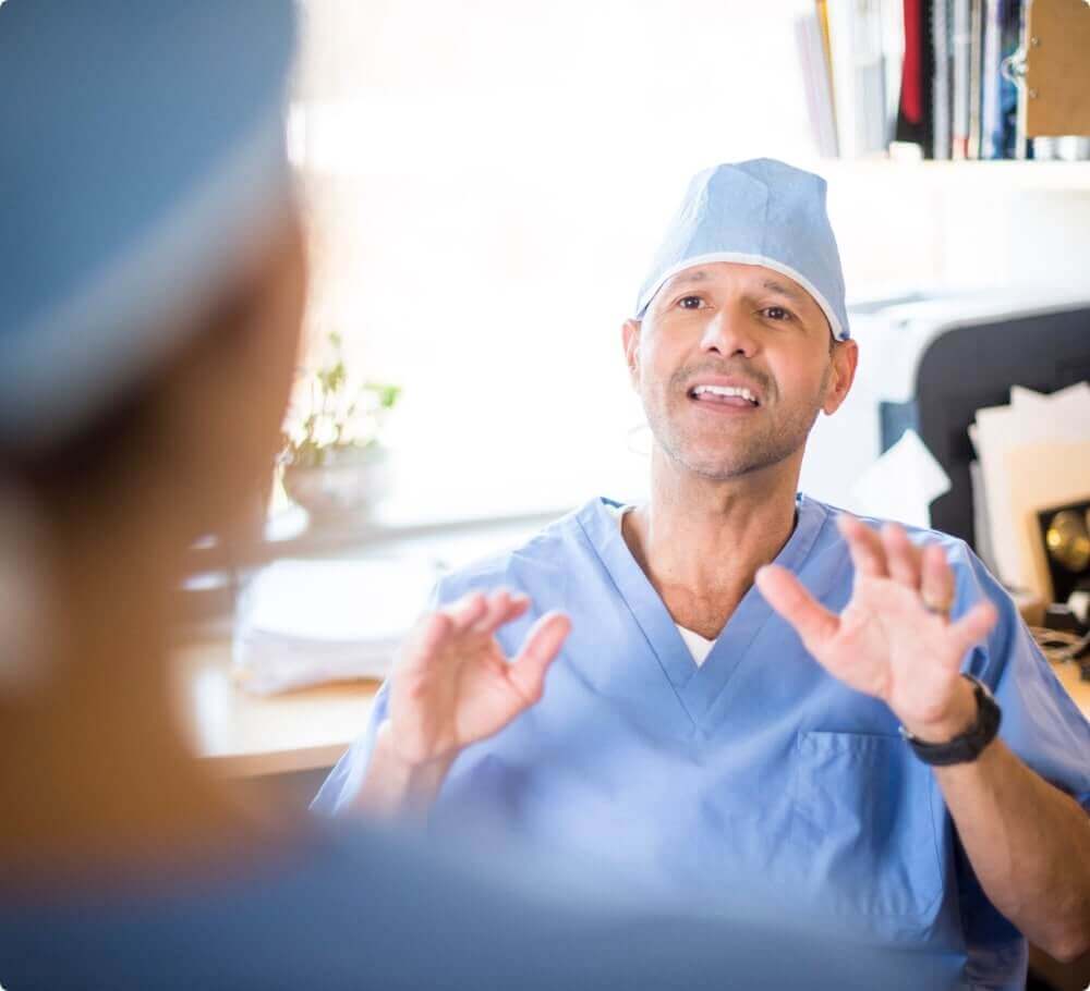 A man in scrubs sitting at a desk talking.