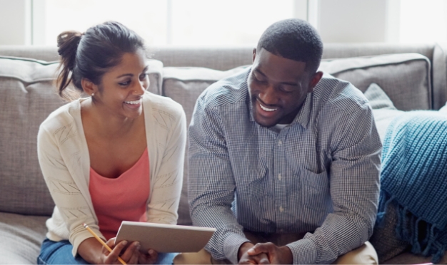 Woman and man sitting on couch smiling at notepad.