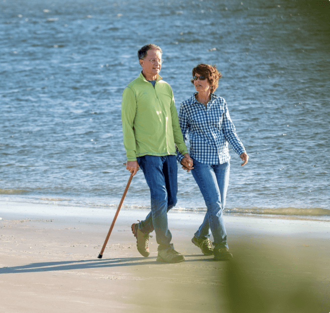 Man with a cane walking with his wife on the beach.