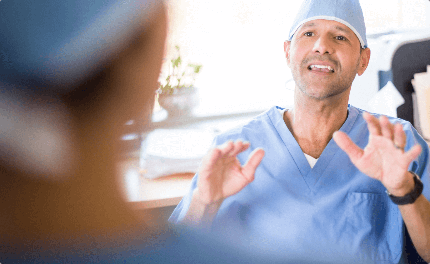 A man in scrubs sitting at a desk talking.