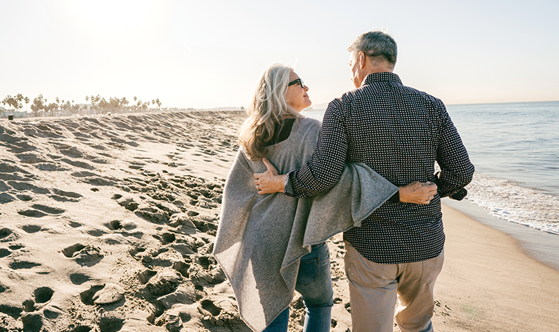 Mature couple walking on beach.