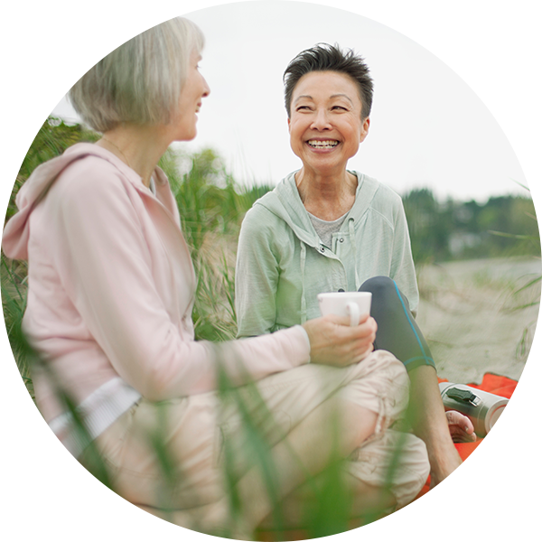 Two middle-aged women sitting outdoors and smiling.