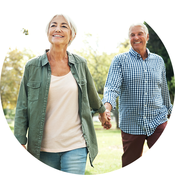 Mature couple holding hands while walking outdoors and smiling.