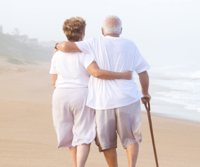 Spinal Cord Stimulation patient Deborah walking on the beach with her husband.