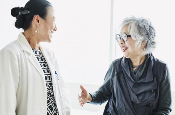 Woman physician and mature woman patient smiling in conversation.
