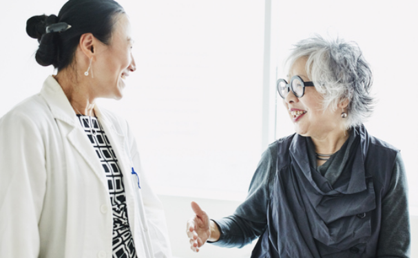 Woman physician and mature woman patient smiling in conversation.