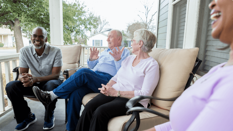 A group of people sitting on a porch talking.