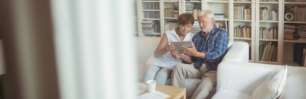 Two adults sitting on couch looking at a tablet together in living room.