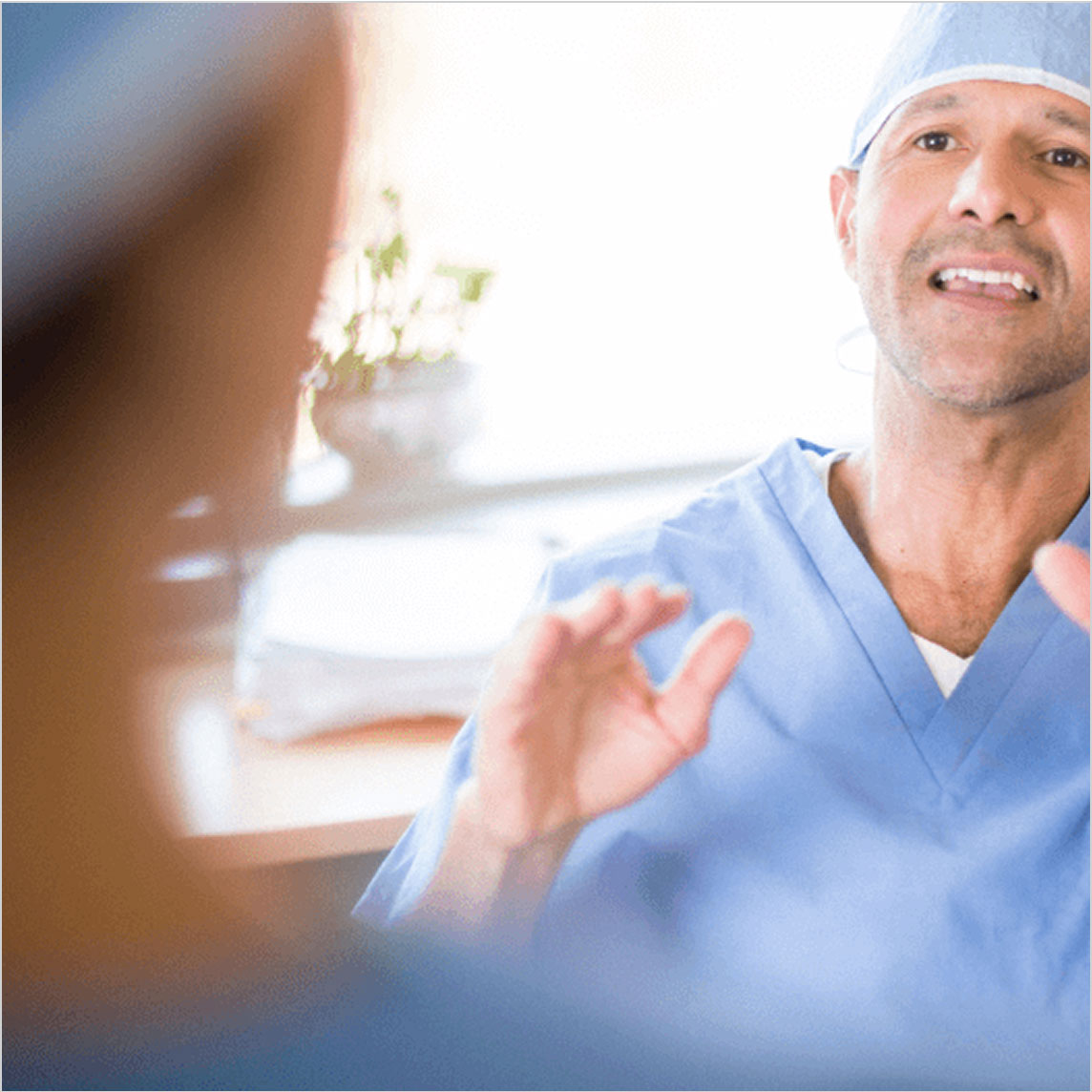 A healthcare provider wearing scrubs gestures while talking to someone in a clinic.