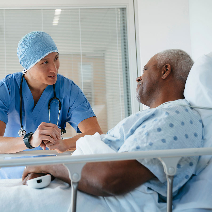 A healthcare provider smiles while talking to a patient in a hospital bed.