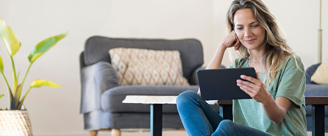 A person sits on the living room floor watching something on a tablet.