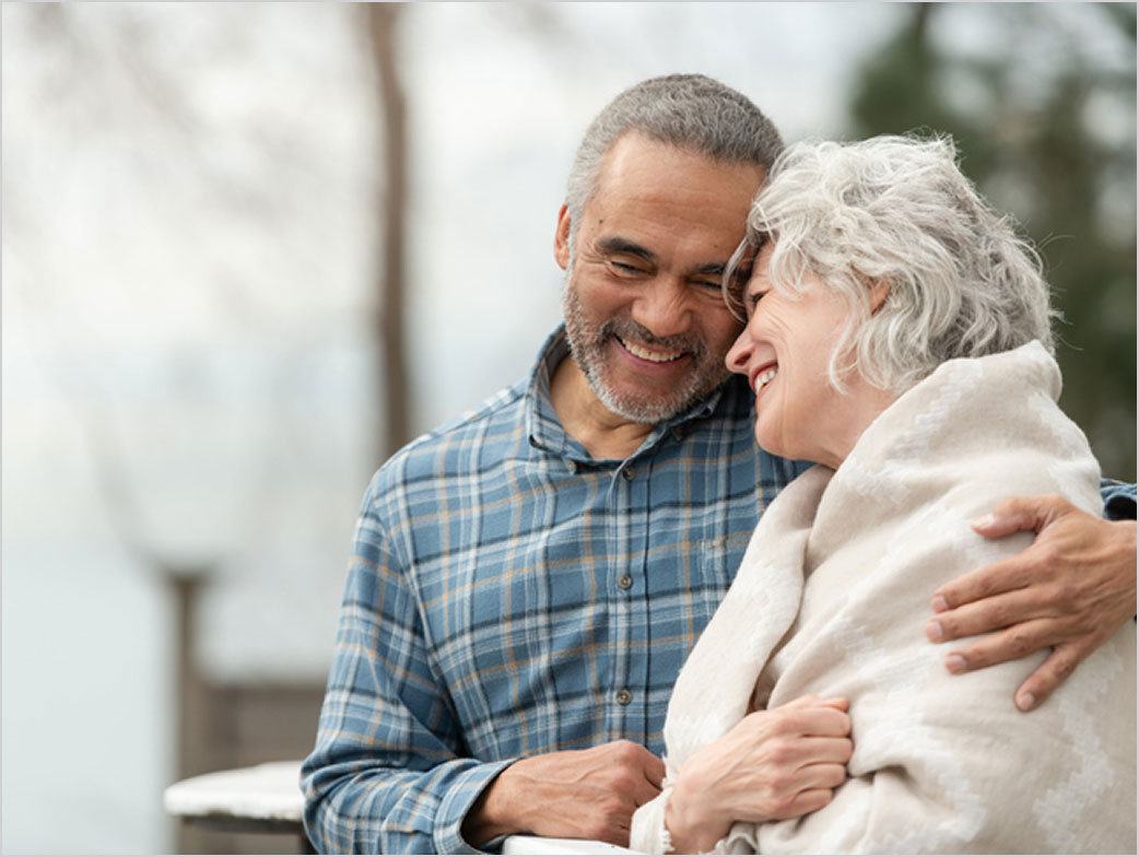 A happy couple smiles while embracing outdoors.