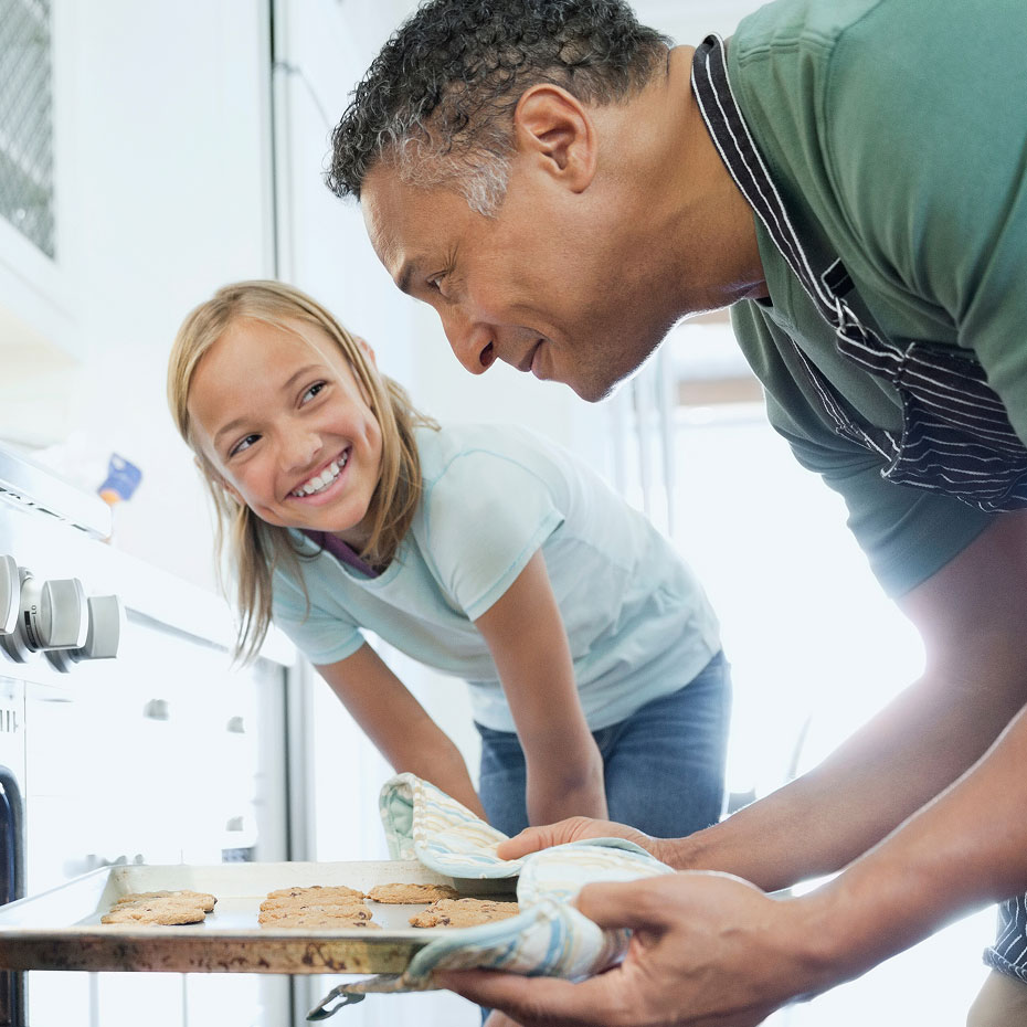 Two people pull freshly baked cookies from the oven on a tray.