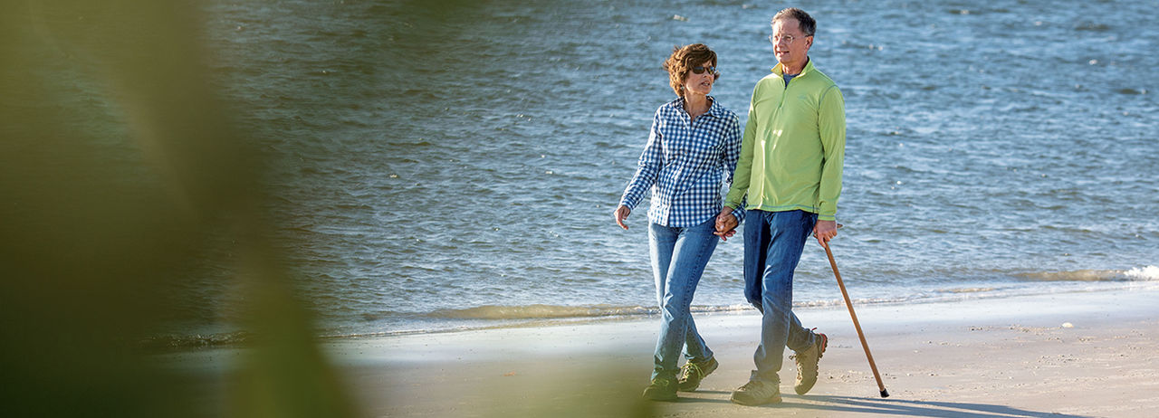 A couple walking hand in hand on the beach with gentle waves behind them.