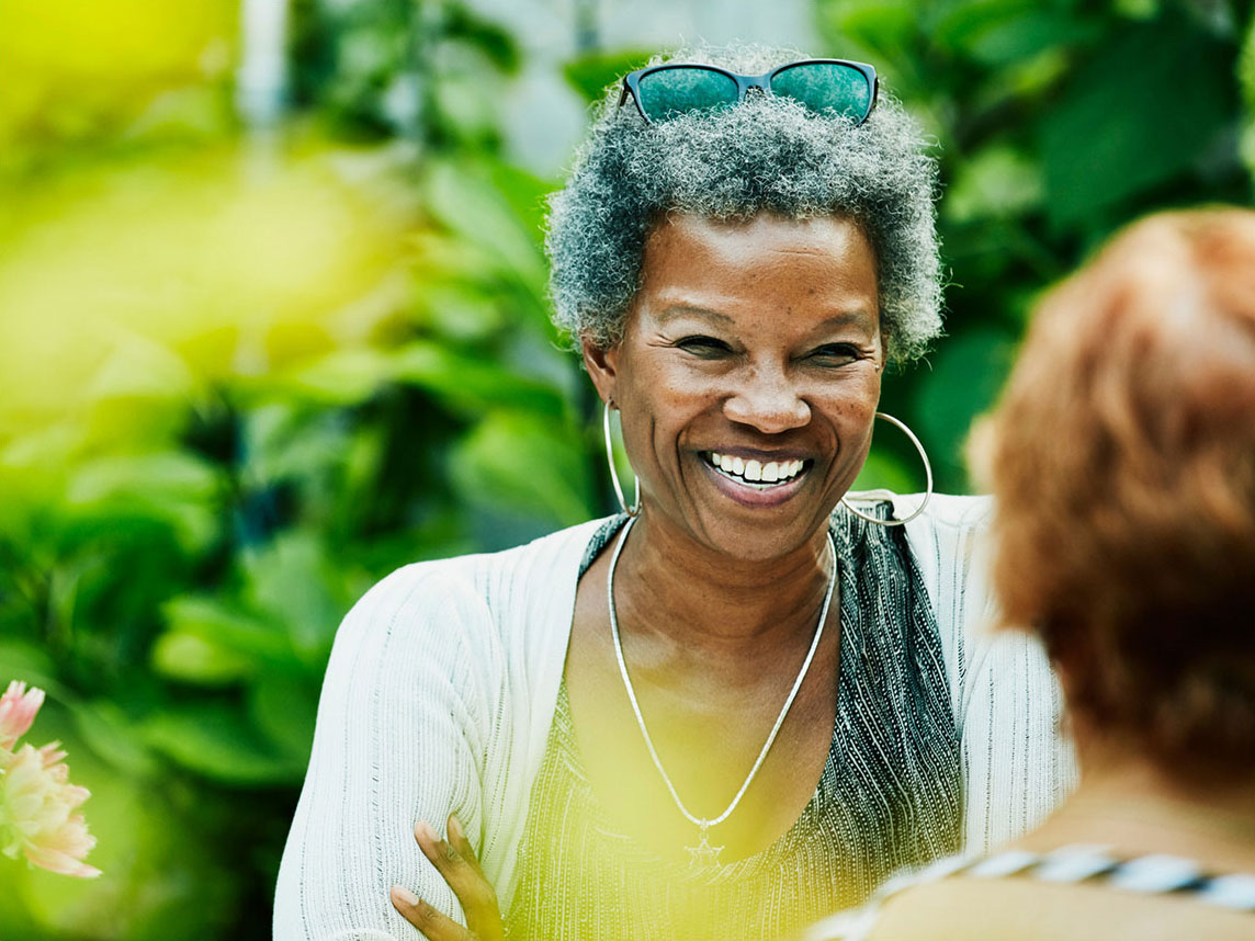 A person smiles while talking outside in a garden.