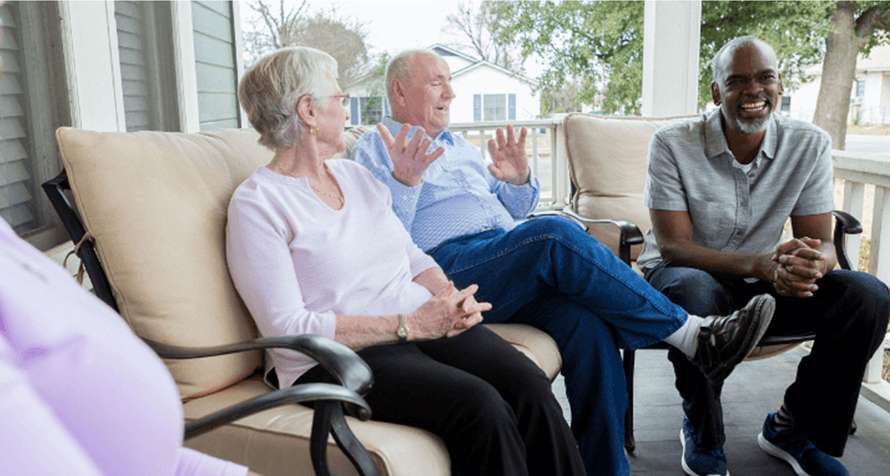 A group of people sits and laughs on a porch during a lively conversation.