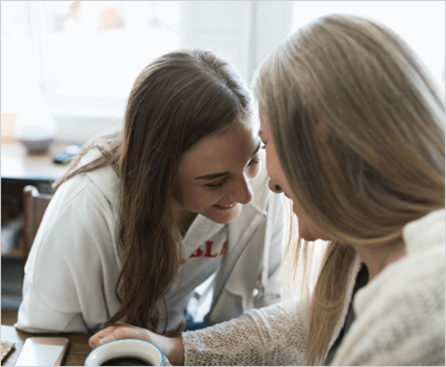 Two people laugh together over a coffee cup.