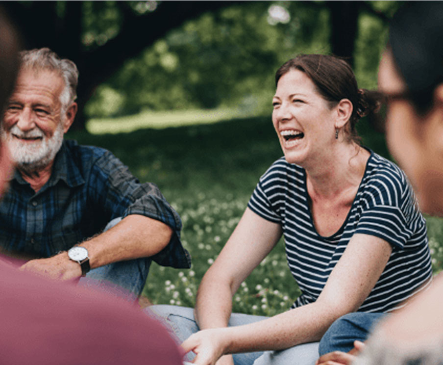 A person laughs as they sit with a group on the grass outside.