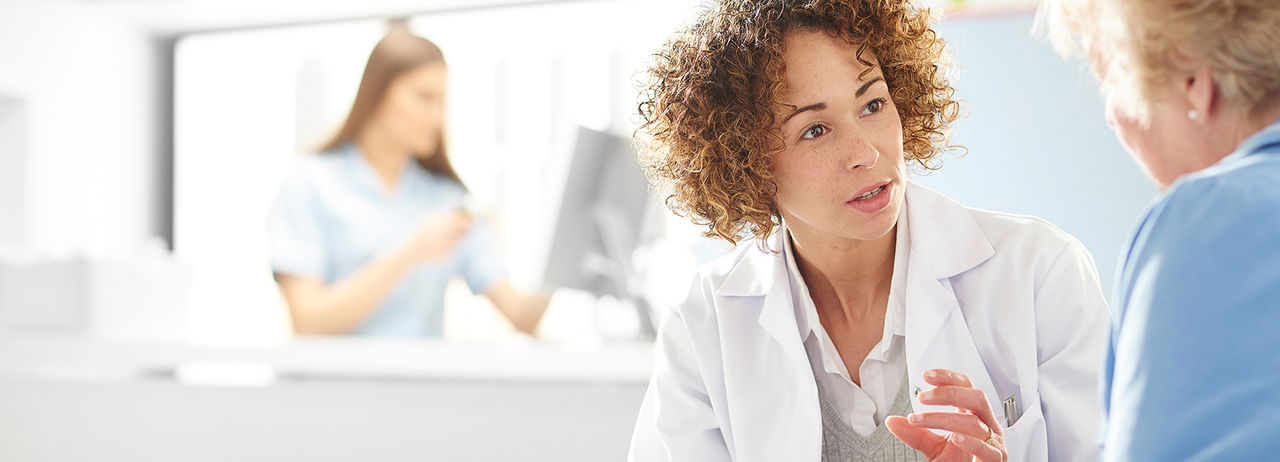 A doctor with curly hair talks to a patient.
